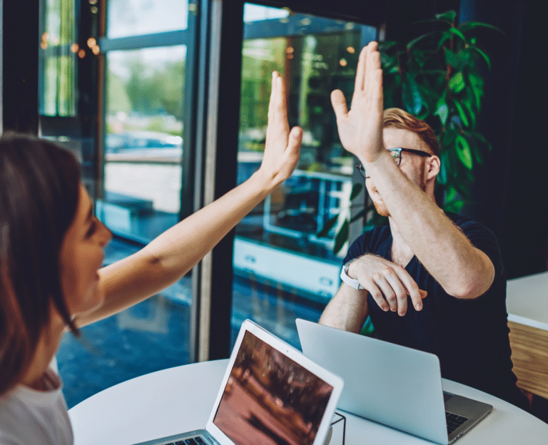 A young man and a young woman high five over their laptops