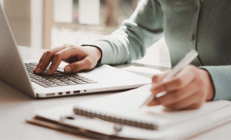 Woman taking notes by a laptop