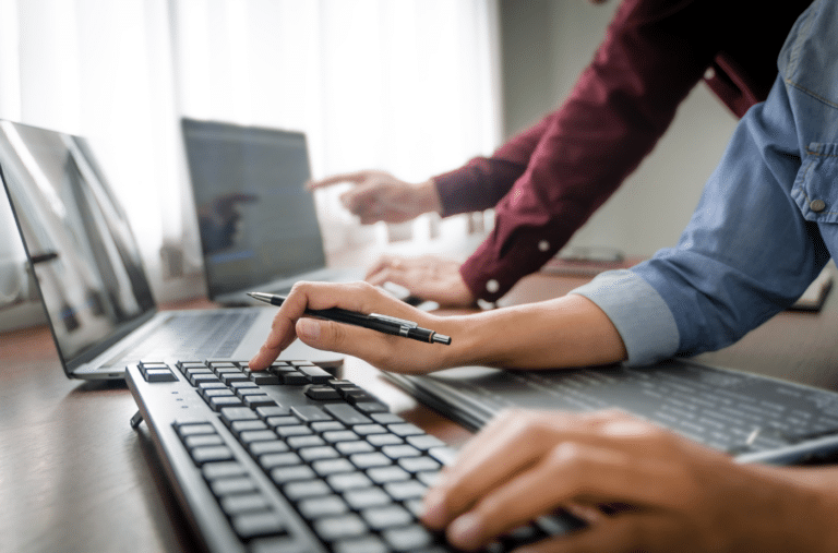 Two people working at a desk on their laptops