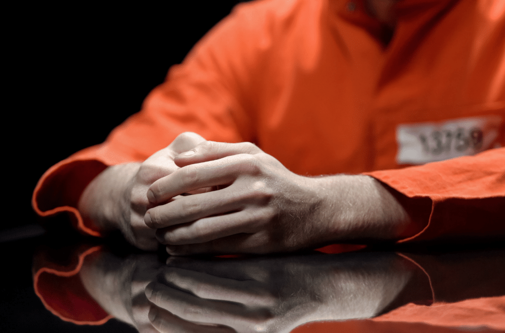 Inmate in orange jumpsuit sitting with their hands folded on a table